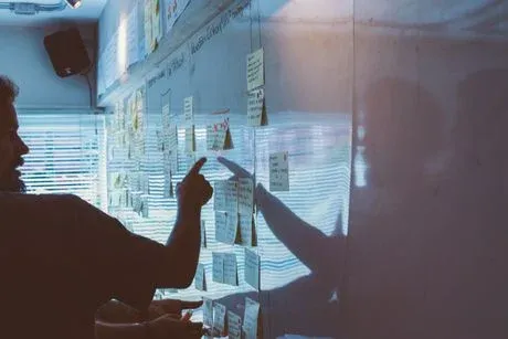 A man pointing with his finger towards a whiteboard with some notes